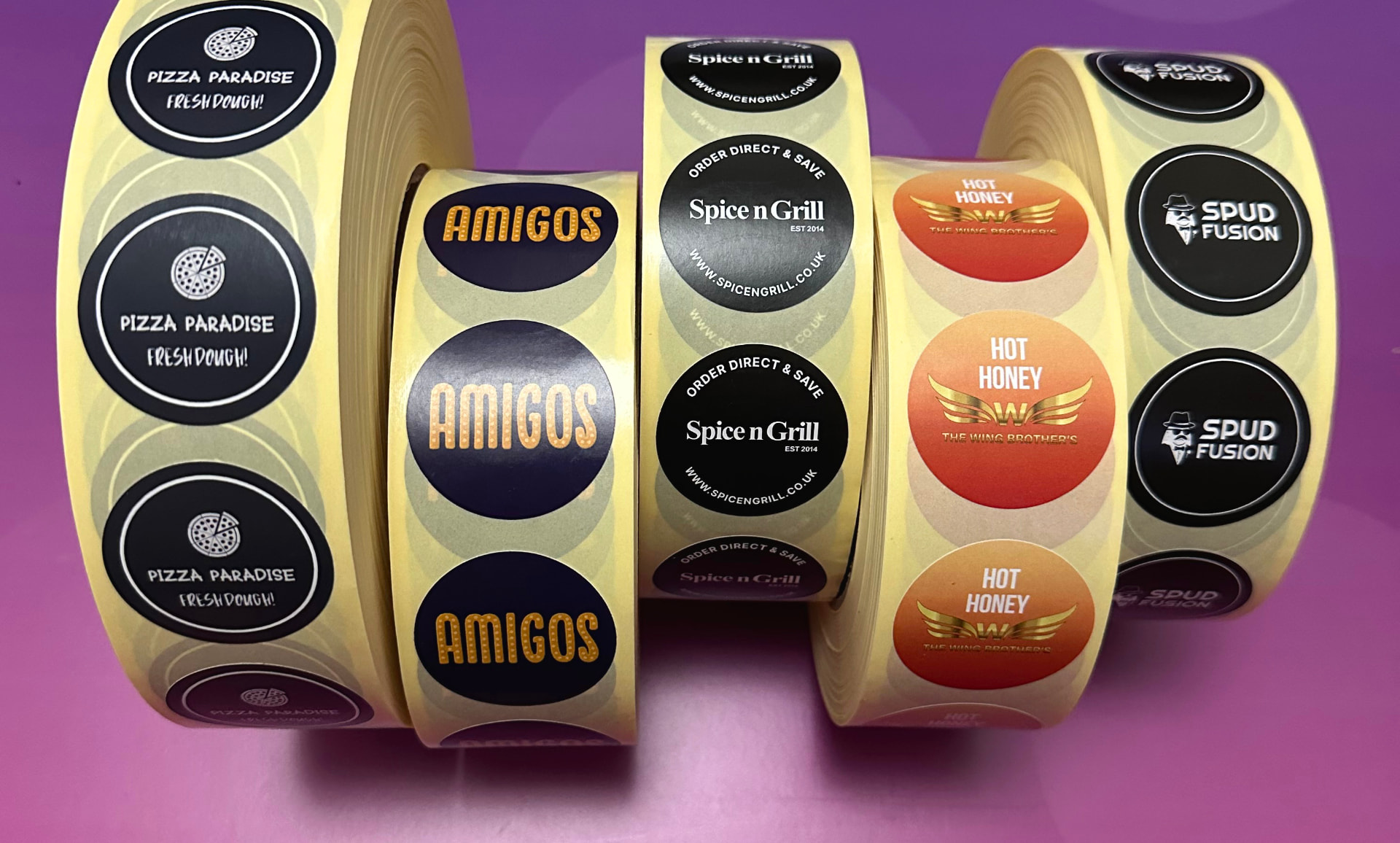 Five rolls of takeaway brand stickers - Pizza Paradise, Amigos, Spice n Grill, Hot Honey and Spud Fusion